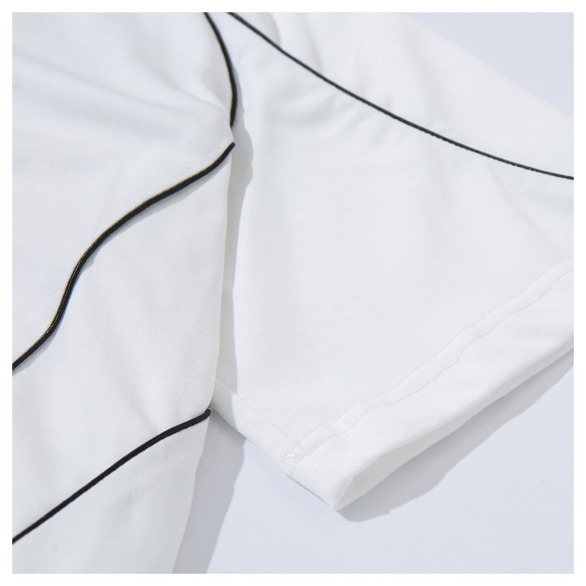 Close-up of the white T-shirt's black-piped raglan seam and sleeve hem stitching.