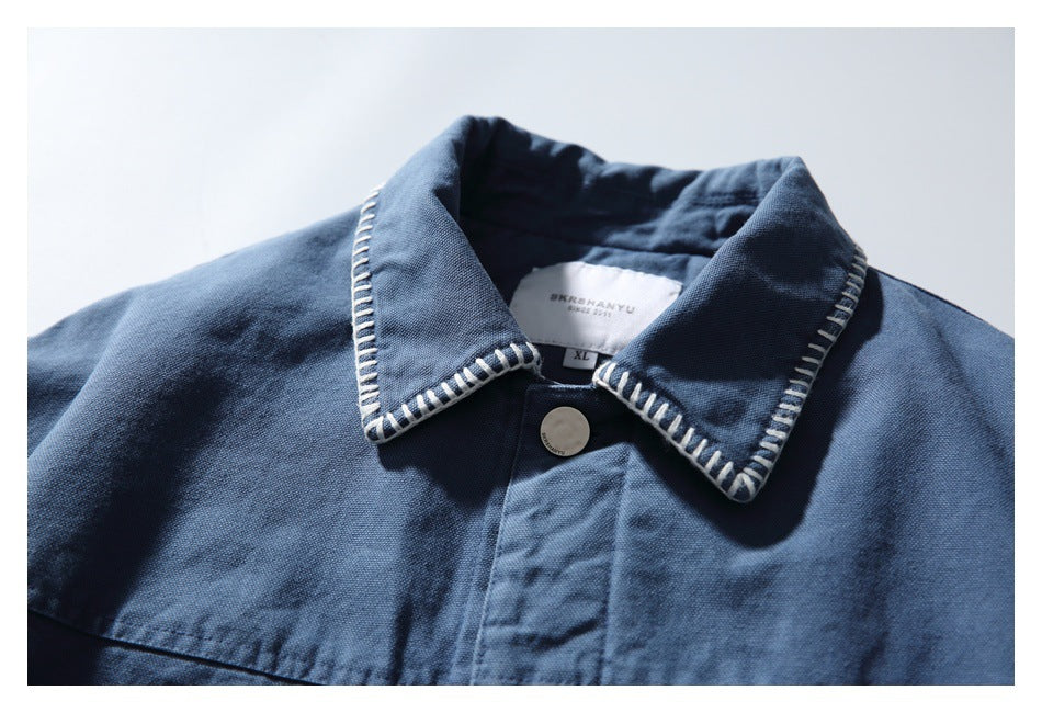 Close-up of a blue jacket collar with white contrast stitching, a metal button, and an inner size label.
