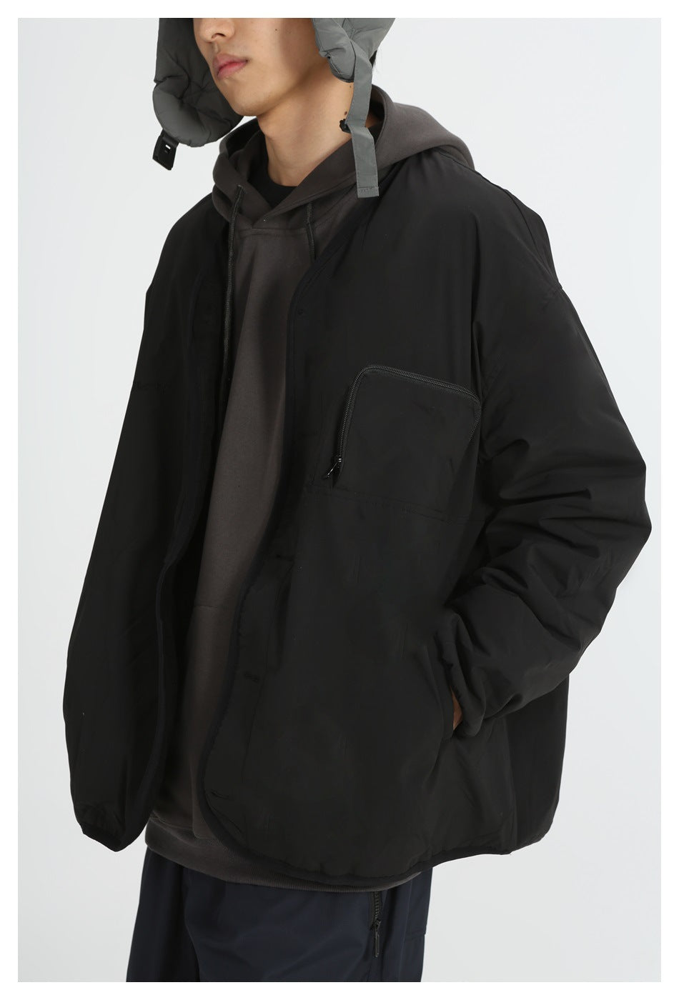 Model wearing a black oversized jacket with a zippered chest pocket over a dark hoodie; front view.
