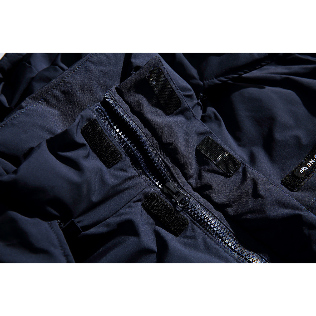 Close-up of a dark navy coat's zipper, pull and hook-and-loop fastening tabs.