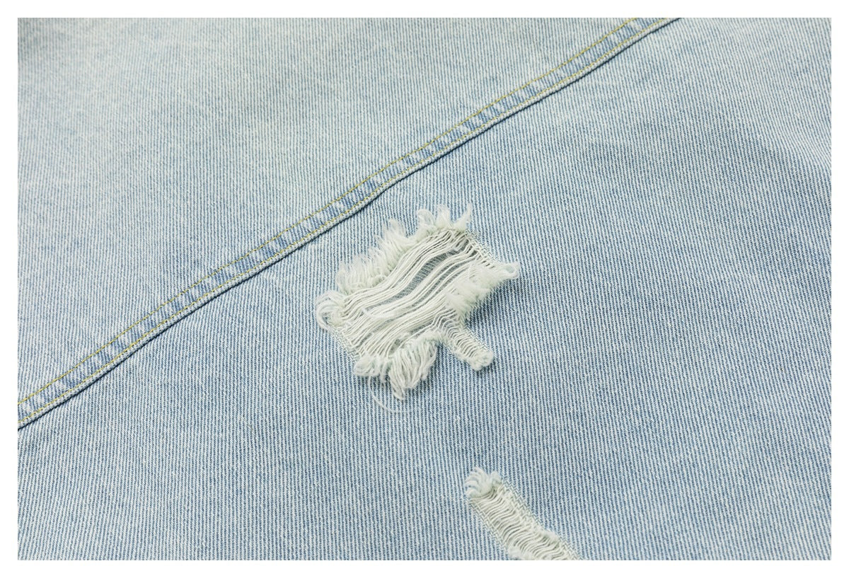 Close-up of light-wash denim showing a large frayed distressed patch and a smaller rip.
