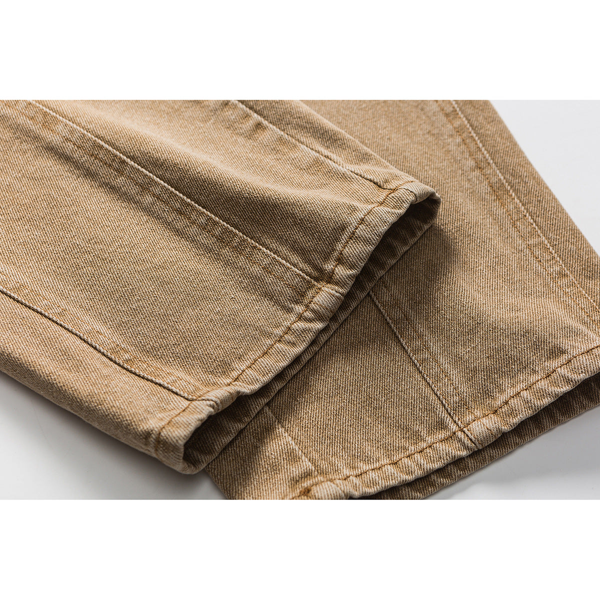 Close-up of the cuff and stitched hem on tan washed jeans.