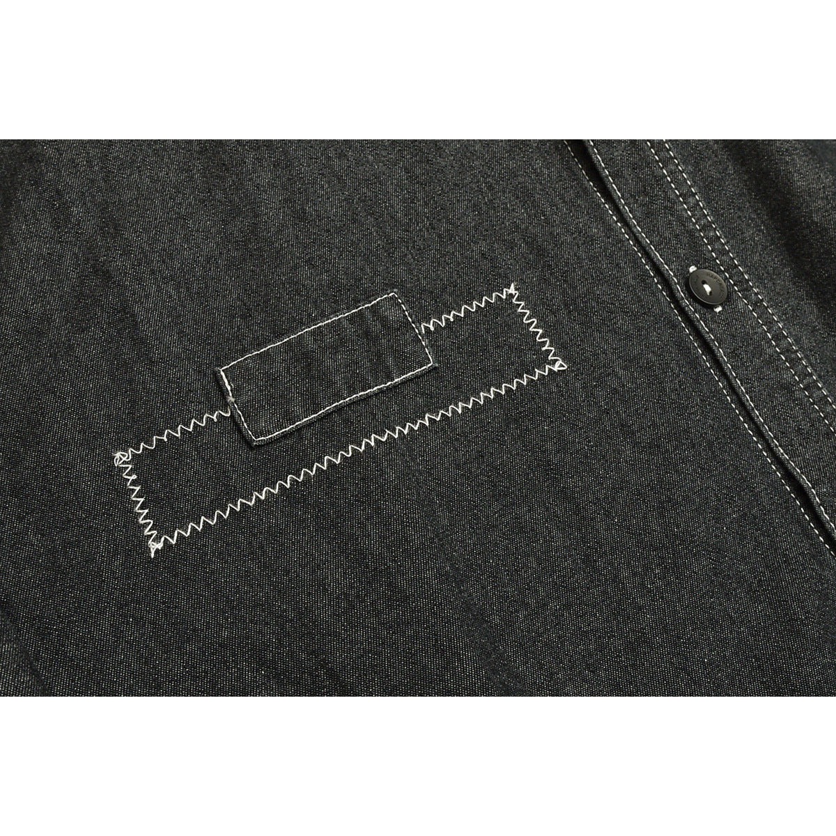 Charcoal shirt detail with a rectangular fabric patch and an angular white zigzag stitch design.