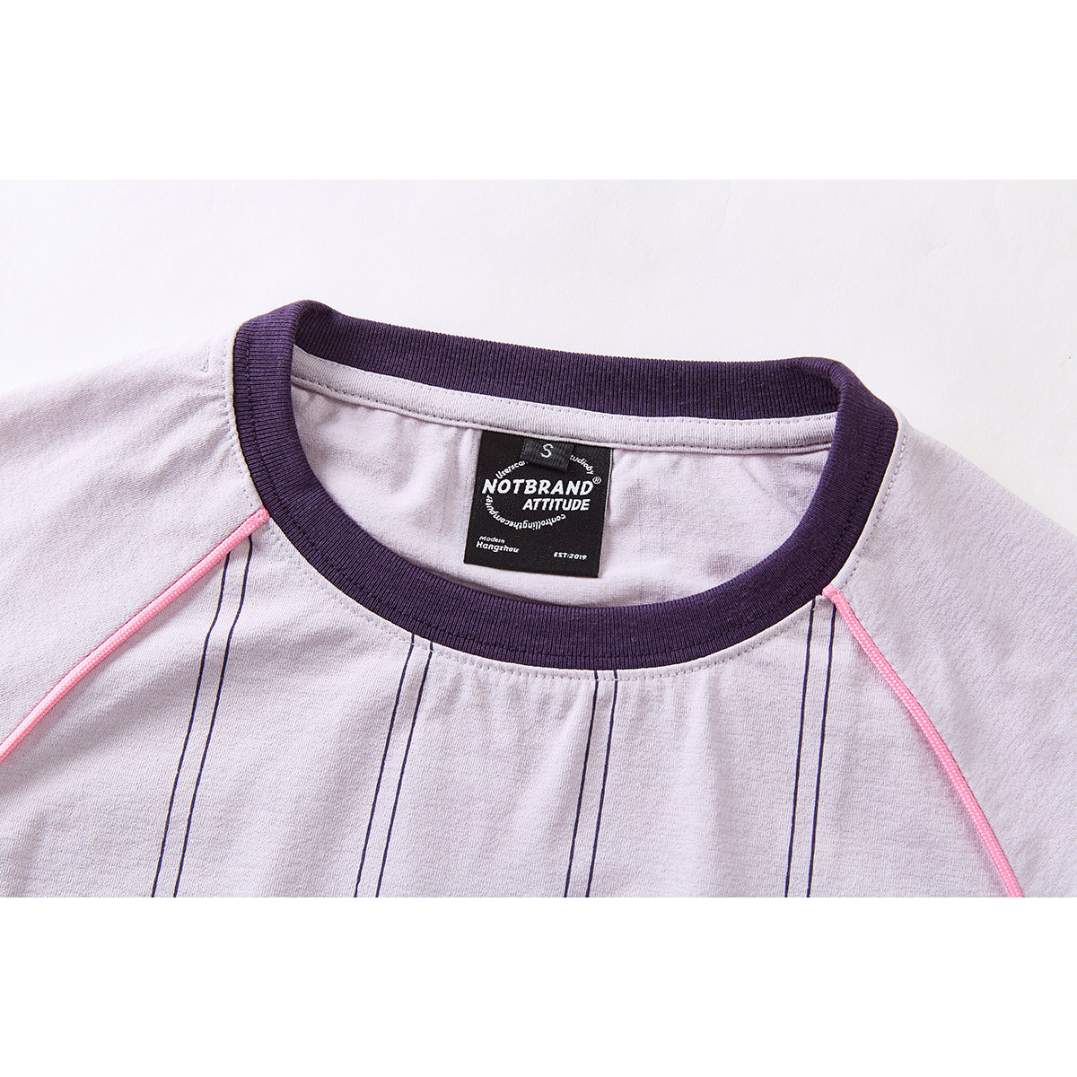 Close-up of a pale lilac shirt neckline with dark purple ribbing, pink piping and a sewn-in label.