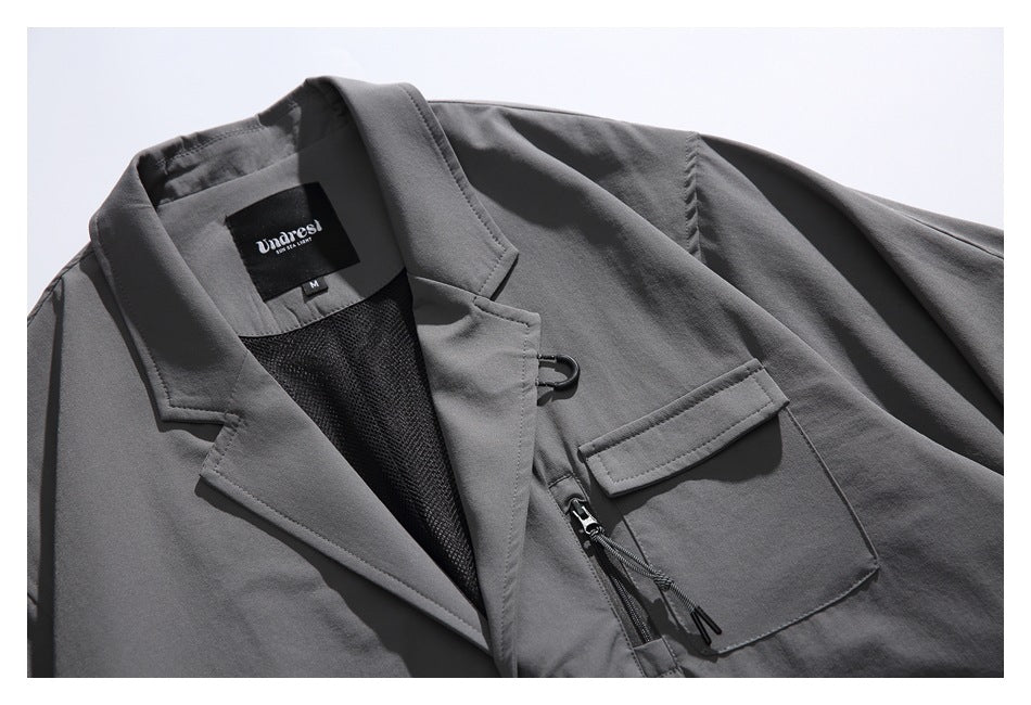 Close-up of the charcoal jacket's notched lapel, mesh lining, chest pocket, zipper, and sewn neck label.