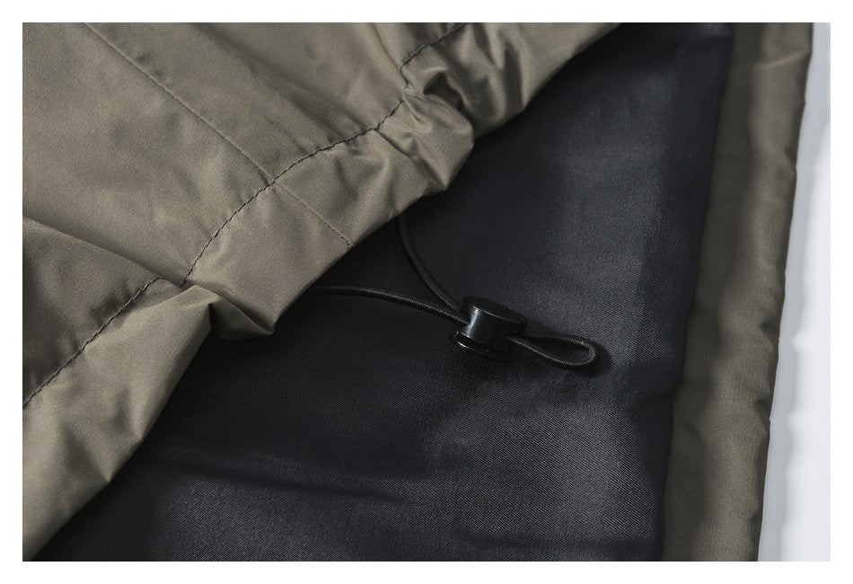 Close-up of a black drawcord toggle at the hem of a gray-olive garment.