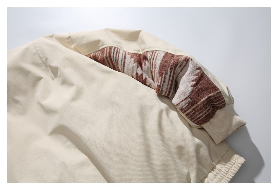 Close-up of a cream garment with a brown-and-cream patterned sleeve panel, ribbed cuff, and gathered hem.