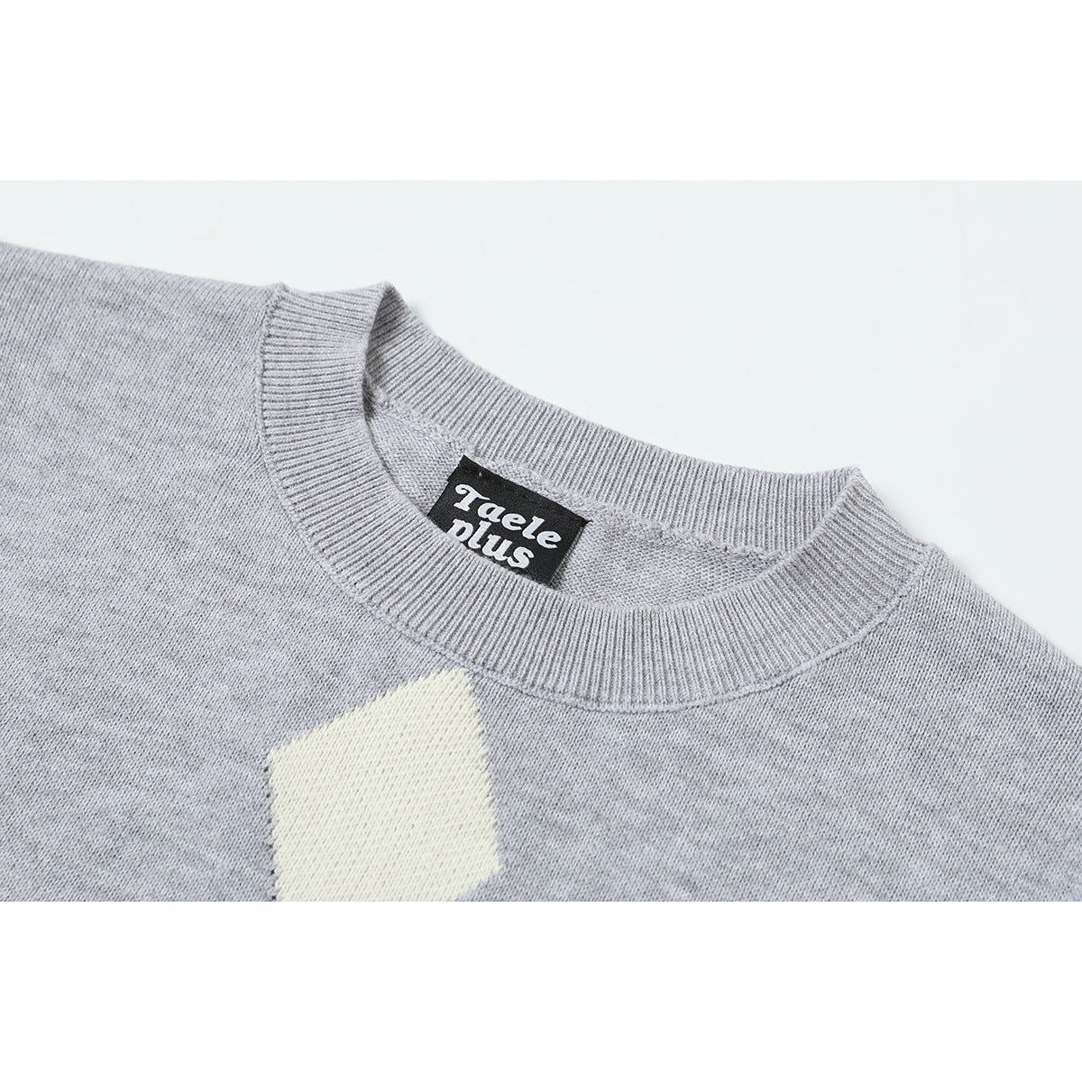 Close-up of the ribbed crew neck and cream diamond detail on a light gray knit sweater.