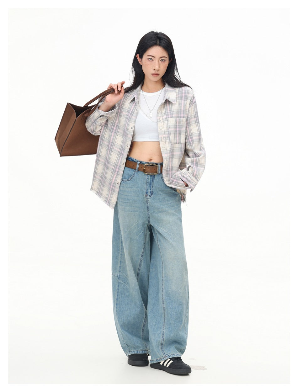 Model wearing an open muted pastel plaid shirt over a white crop top with wide-leg blue jeans.