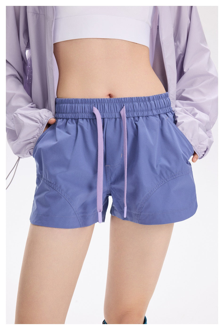 Model wearing periwinkle-blue running shorts with an elastic waist, long lavender drawstrings and curved front pockets.