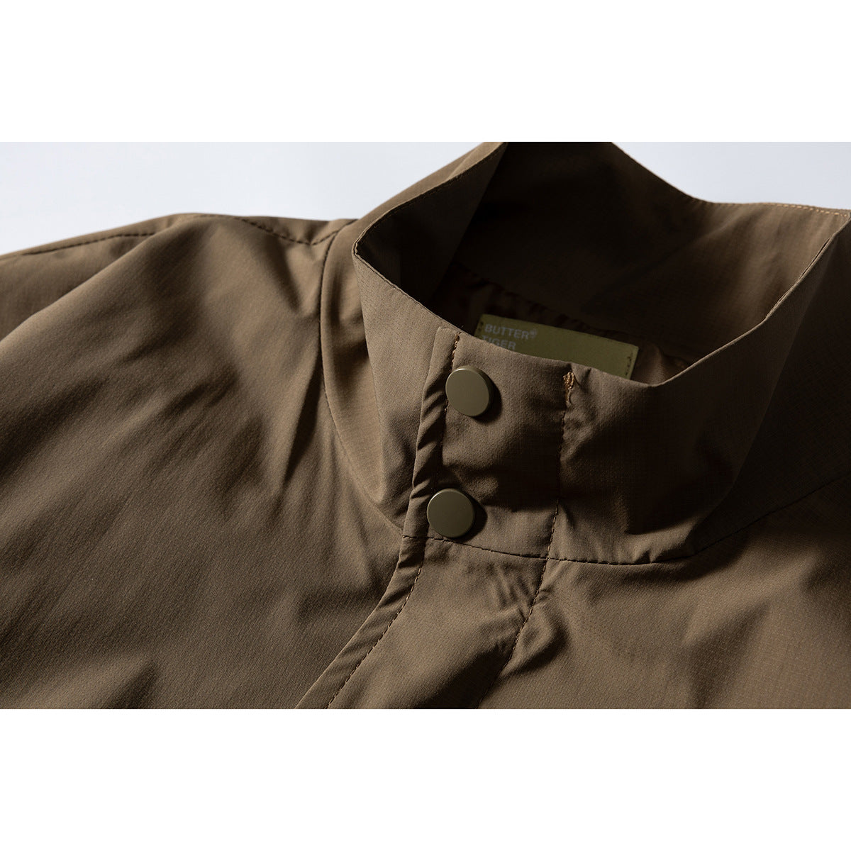 Close-up of a brown jacket's stand collar, two snap buttons, stitching, and partially visible inner label.