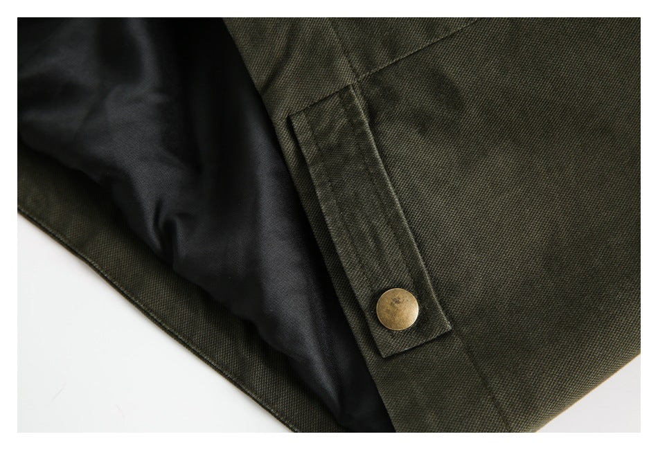 Close-up of an olive jacket cuff tab with a brass-toned snap and black lining.
