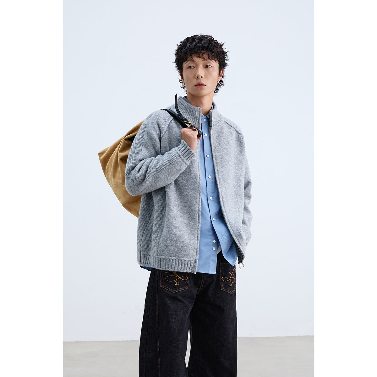 Model wearing a light gray zip-front knit jacket with a ribbed stand collar, carrying a tan bag.