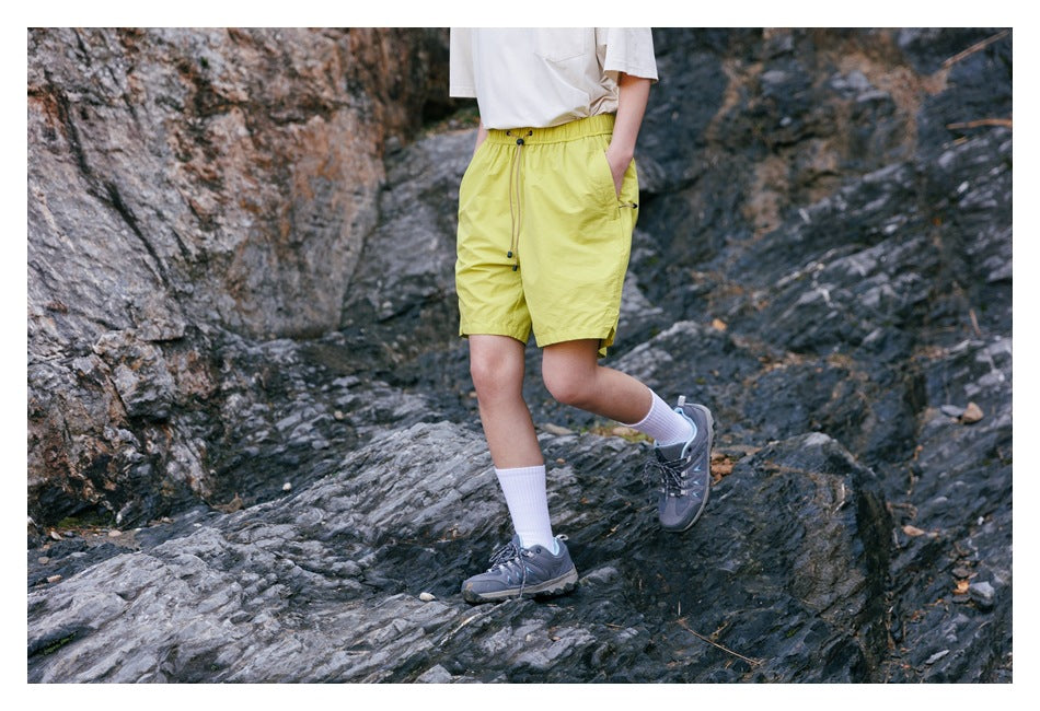 Cropped view of a person wearing bright yellow-green shorts with an elastic drawstring waist while stepping over rocks.