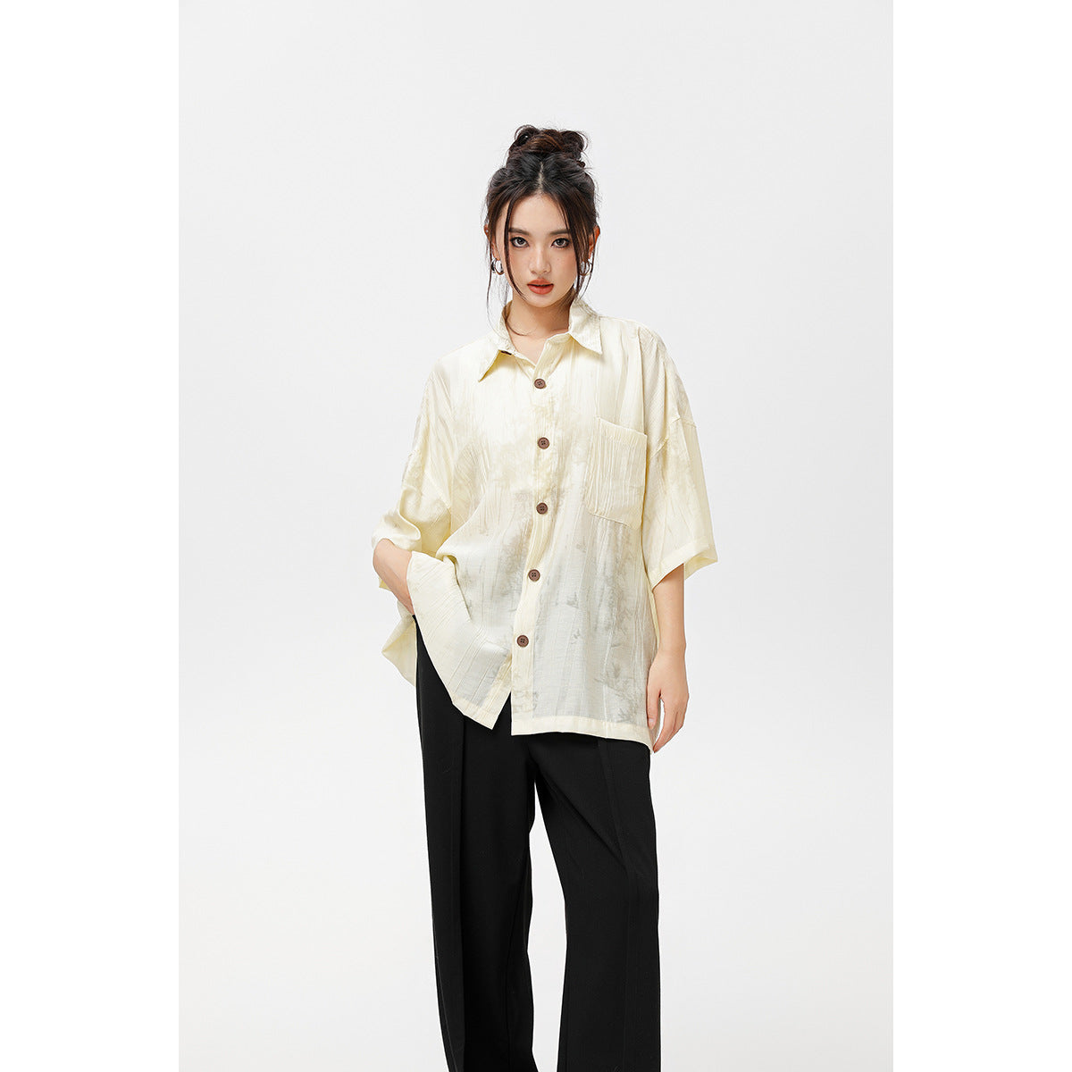 Closer view of a model wearing an oversized ivory button-up shirt with brown buttons and a chest pocket.