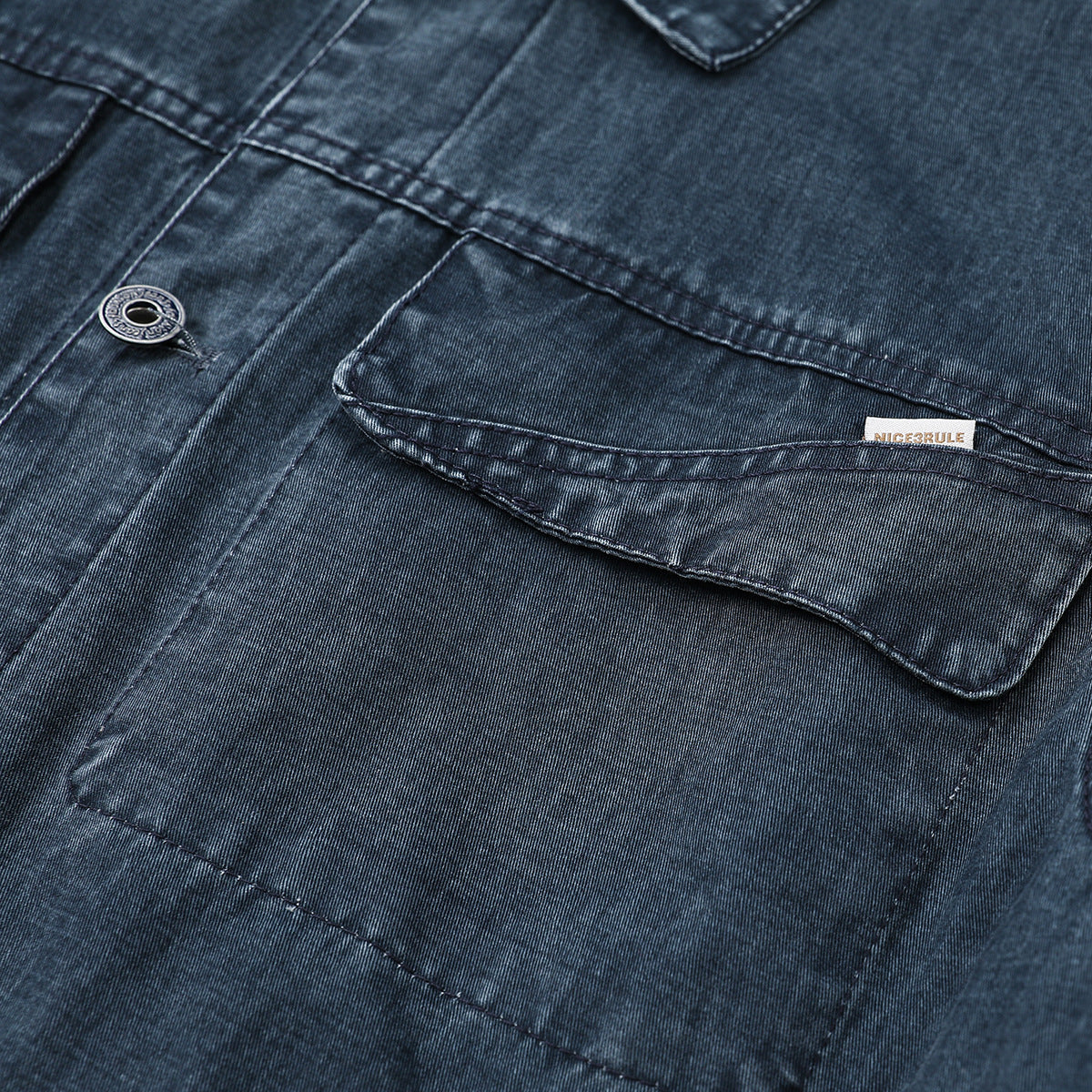 Close-up of a dark blue denim jacket chest pocket, button, and small sewn label.