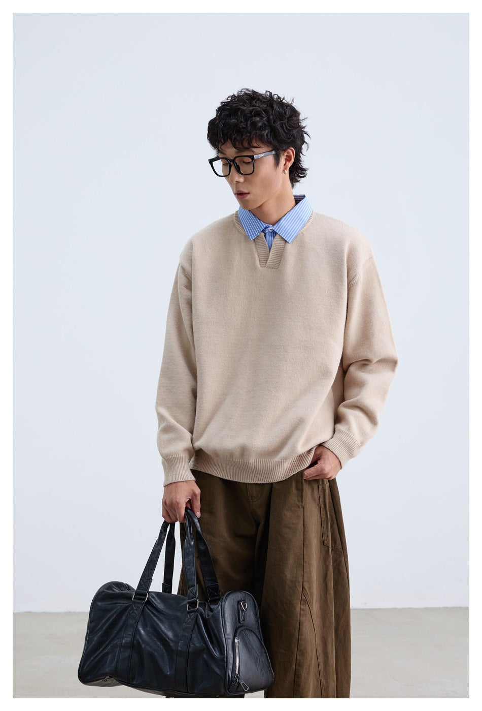 Front view of a model wearing a relaxed beige V-neck sweater over a blue striped shirt.