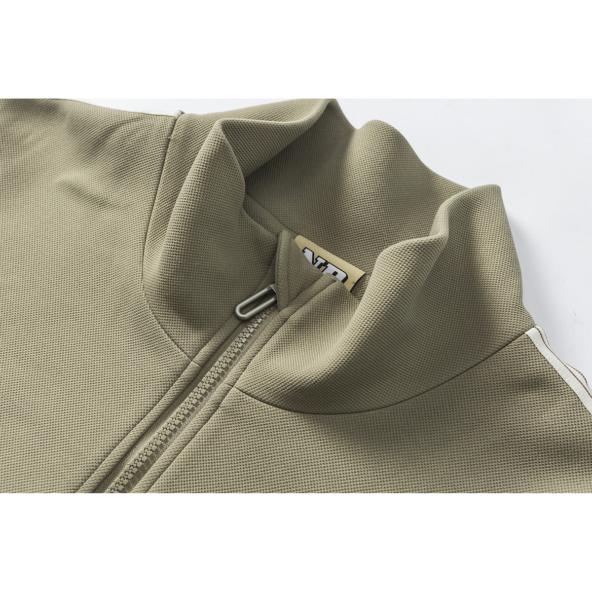 Close-up of an olive zip jacket’s raised collar, zipper and partial inner neck label.