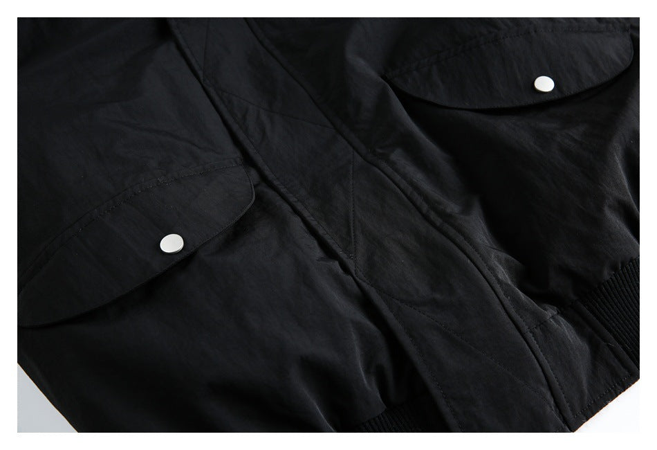 Close-up of a black jacket front with two snap-flap pockets and a central fastening placket.