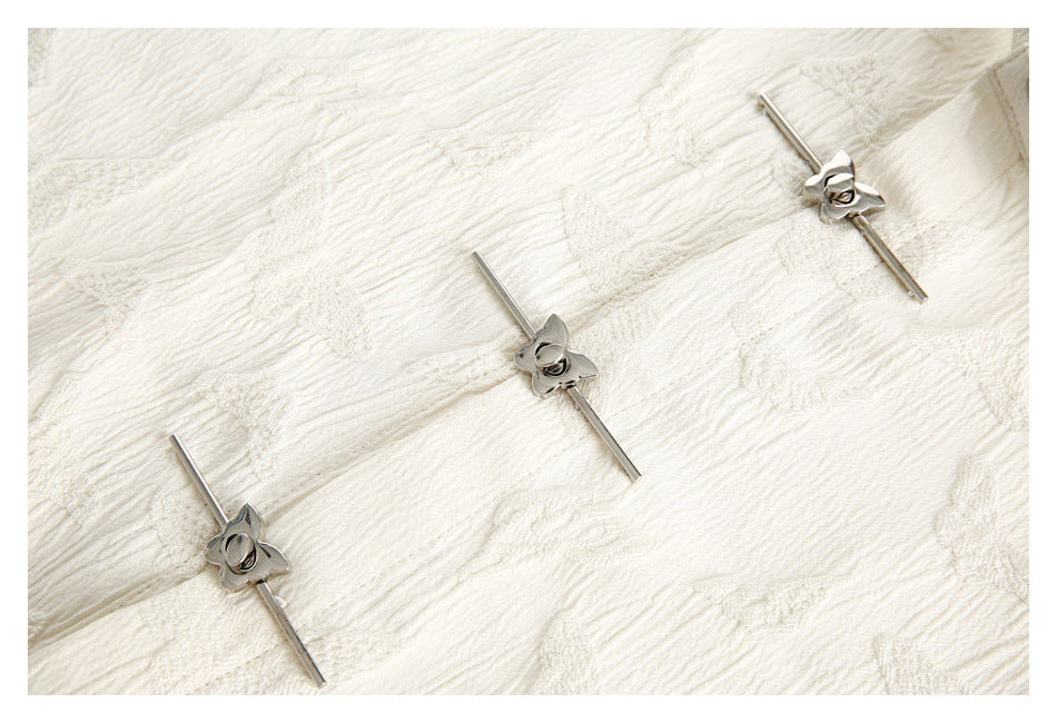 Ivory textured fabric with three silver flower-shaped decorative fasteners.