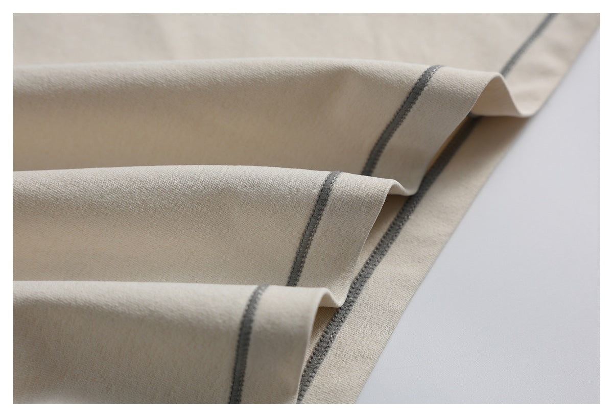 Close-up of folded light beige garment fabric with dark gray overlock stitching along the edges.