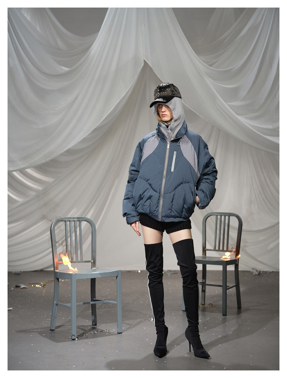 Model wearing a blue-gray padded jacket with dotted shoulder panels, a gray hood and black thigh-high boots.