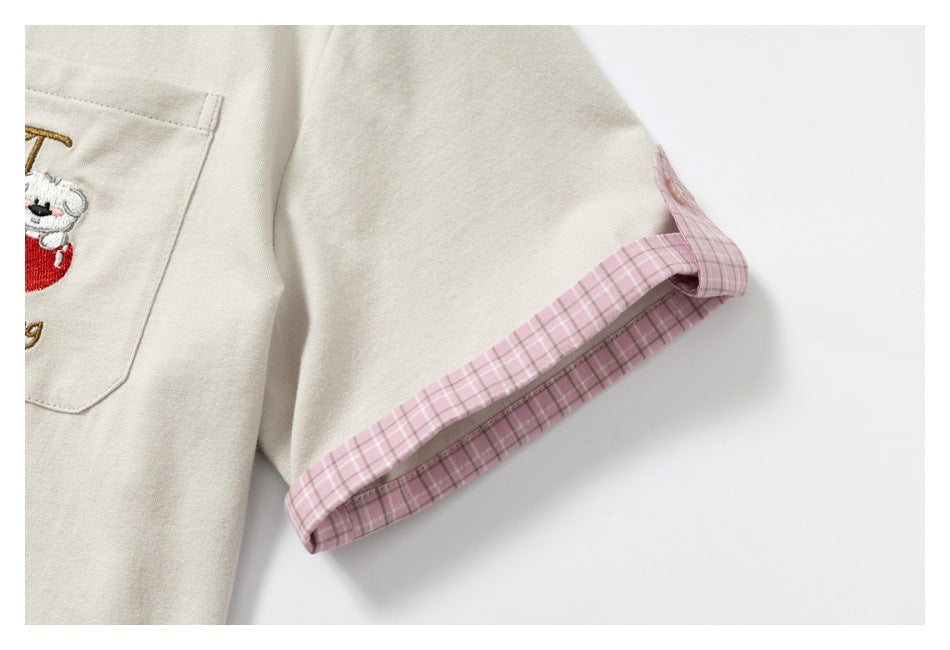 Close-up of an ivory garment sleeve with a pink plaid cuff and part of an embroidered chest pocket.