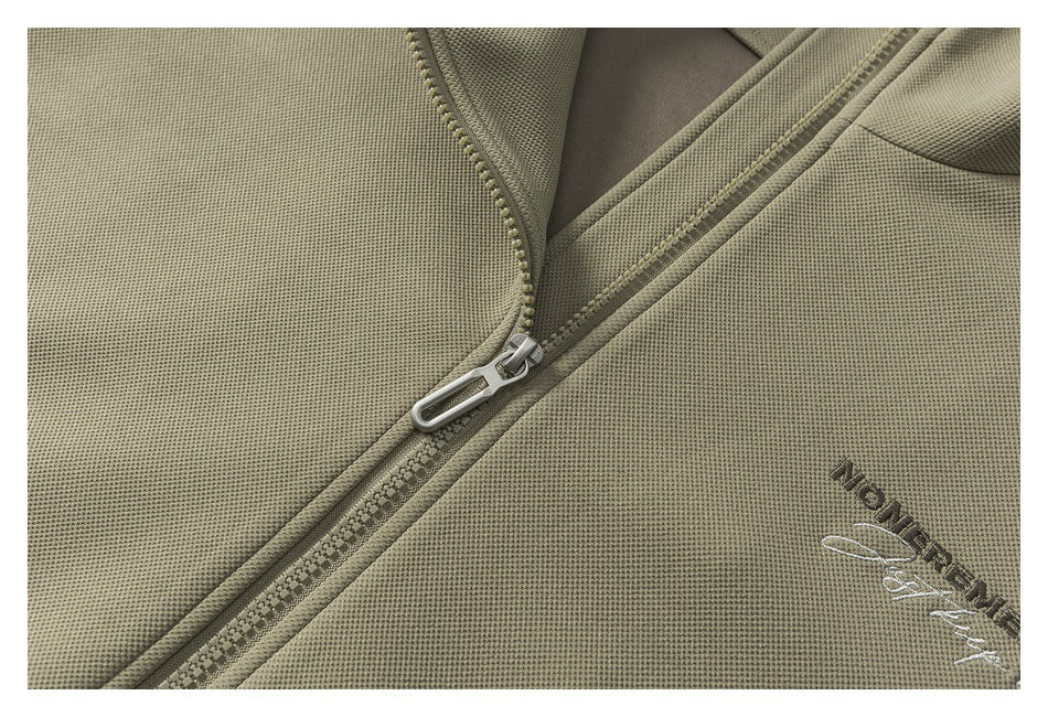 Close-up of an olive jacket's front zipper, textured fabric, and embroidered lettering.