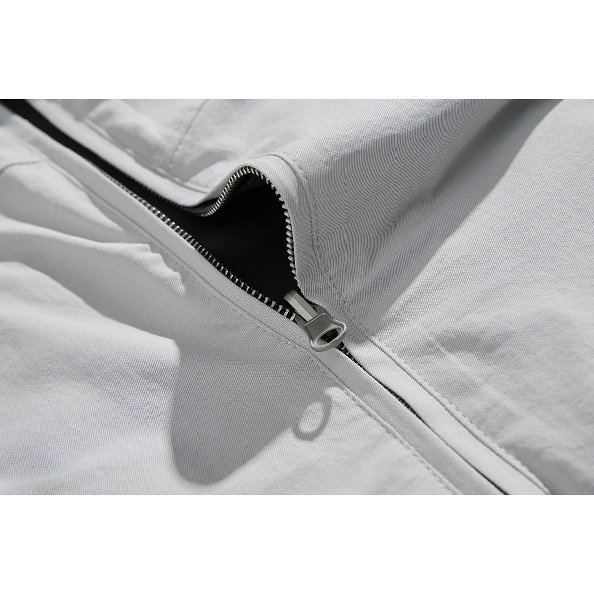 Close-up of the light gray jacket's partially open front zipper and metal pull.