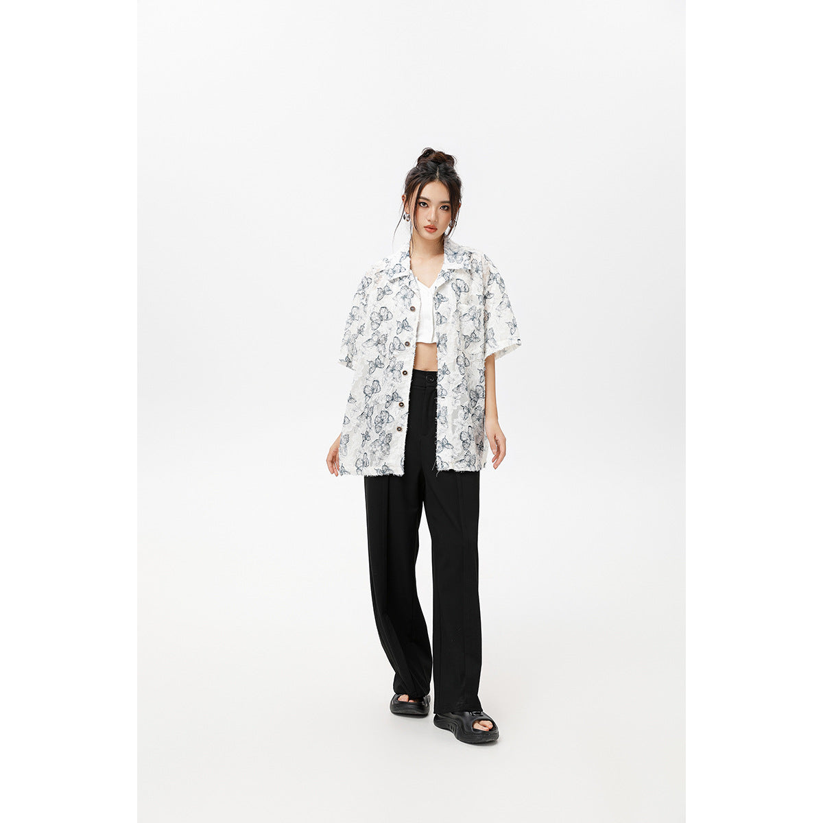 Model wearing an oversized white short-sleeve button-up shirt with gray-blue butterfly prints and black trousers.