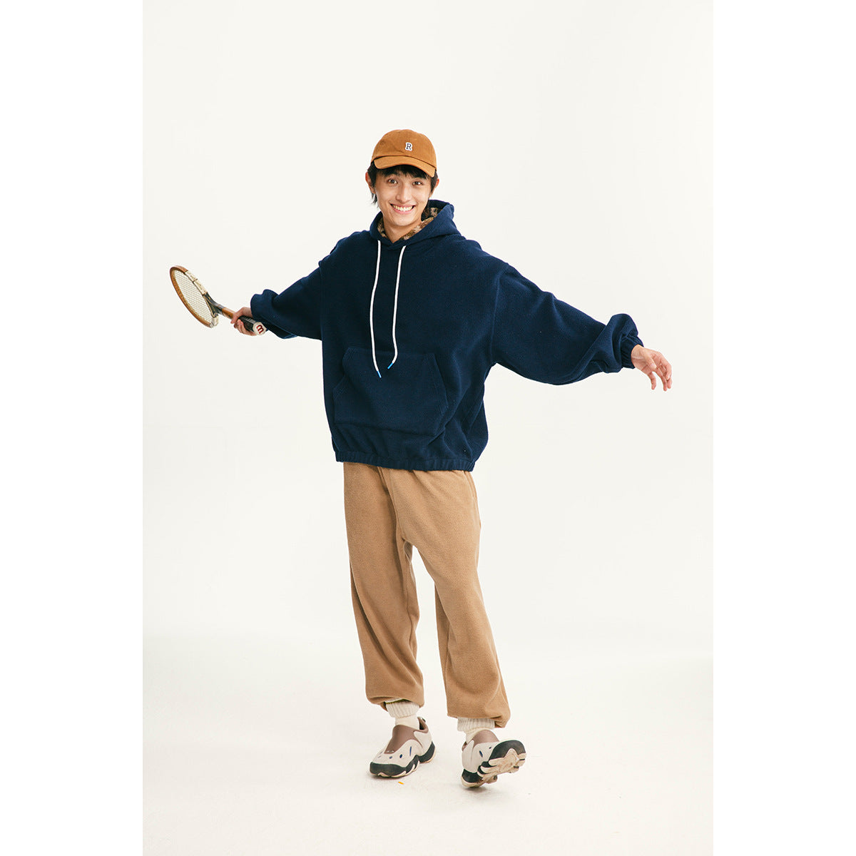 Model wearing an oversized navy pullover hoodie with white drawstrings and a front pocket, paired with tan pants.