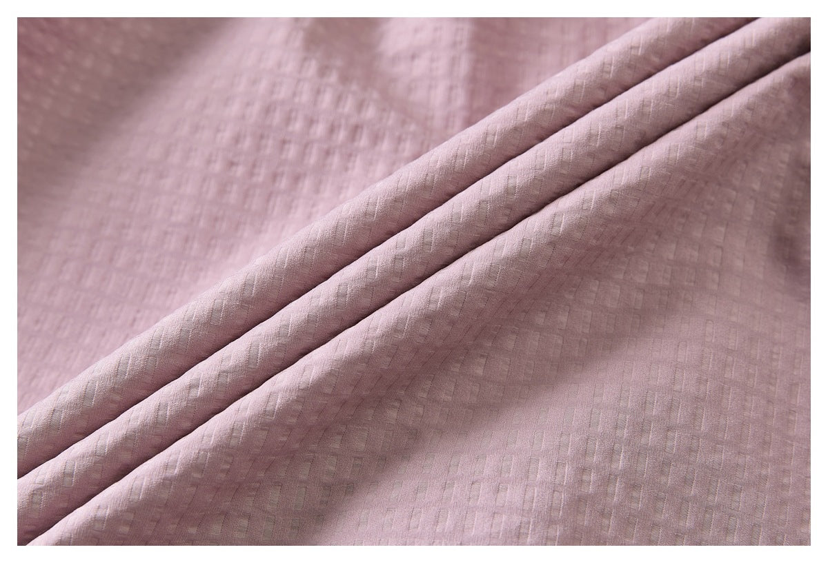 Close-up of dusty rose fabric with a subtle woven geometric texture and folded layers.