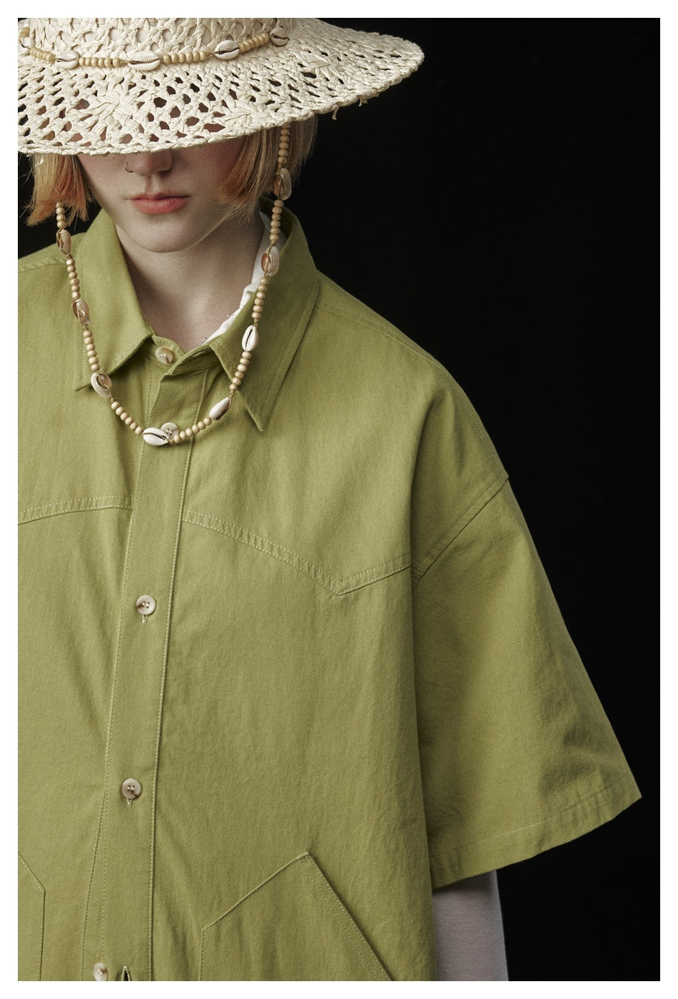 Close-up of a model wearing an olive-green button-up shirt with a pointed collar and chest seams.