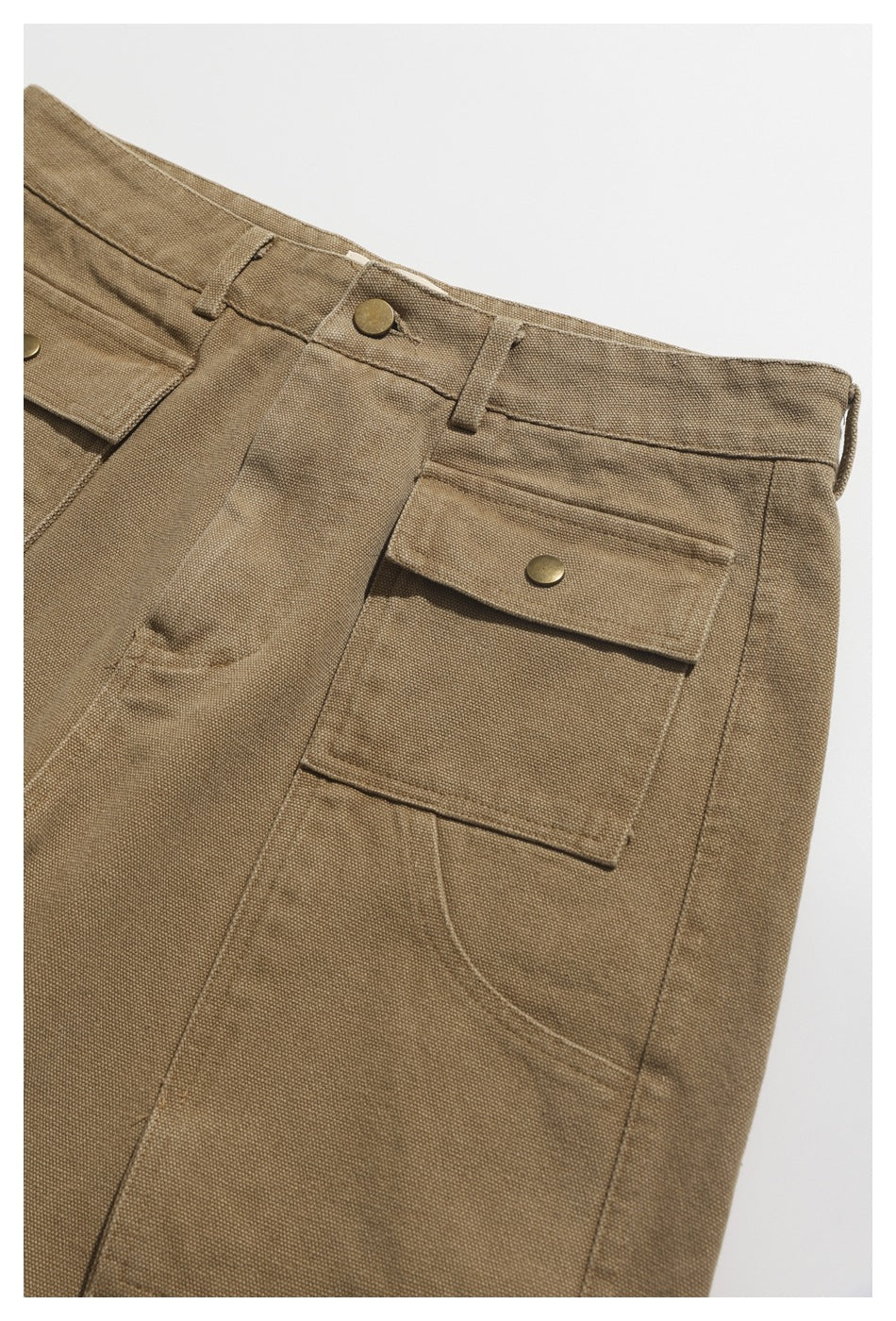 Close-up of tan utility trousers showing the waistband, belt loops, and a large snap-flap pocket.