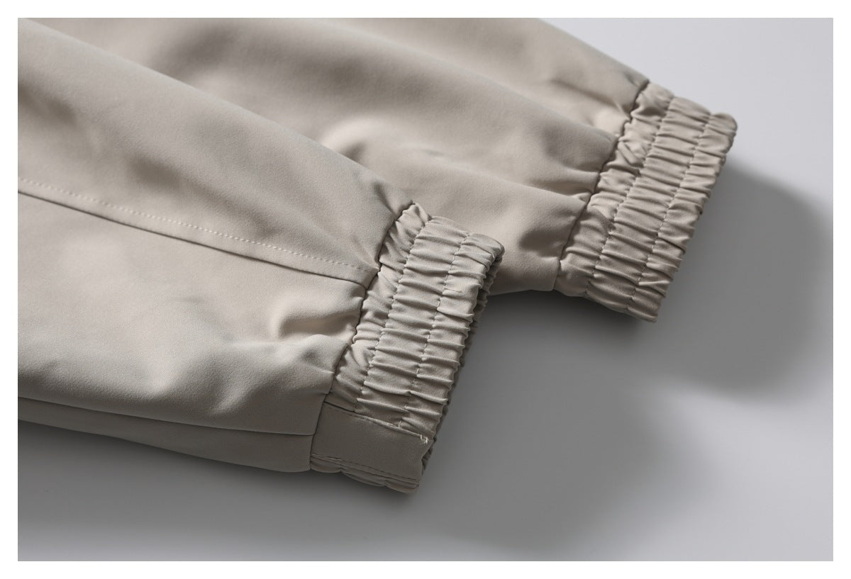 Close-up of taupe trouser legs with gathered elastic ankle cuffs and visible stitching.