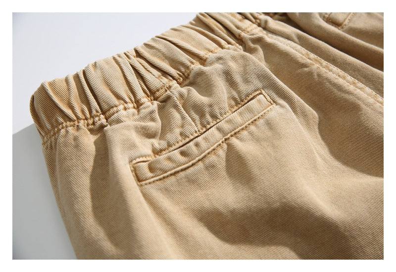 Close-up of tan trousers showing an elastic waistband, angled pocket, and visible stitching.