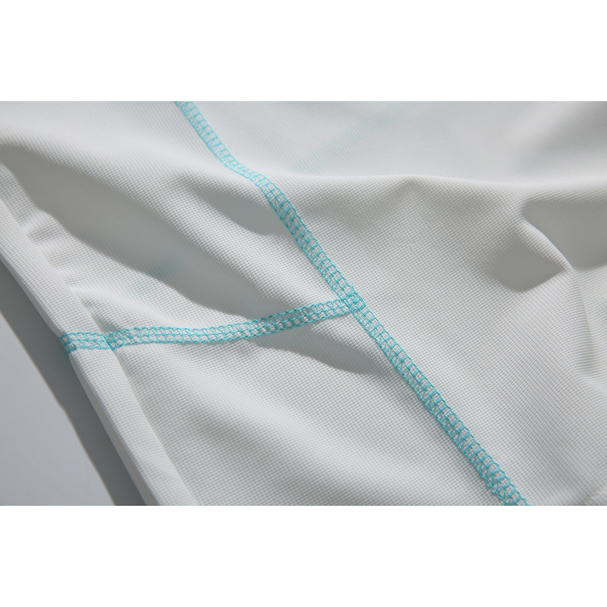 Close-up of white textured fabric with turquoise overlock stitching crossing at the seams.