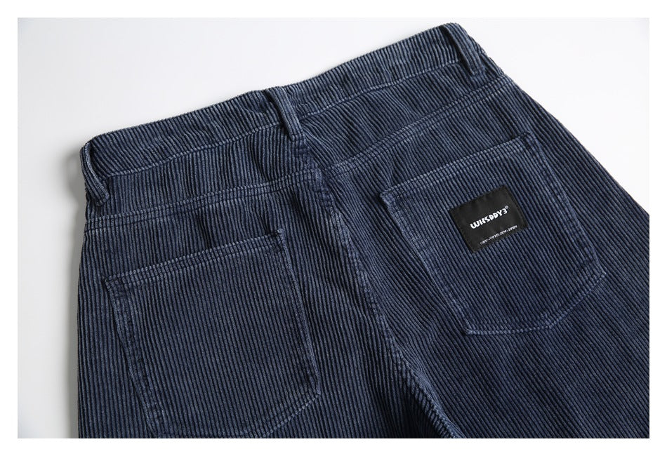 Close-up of navy ribbed corduroy trousers showing the waistband, belt loop, and two back pockets.