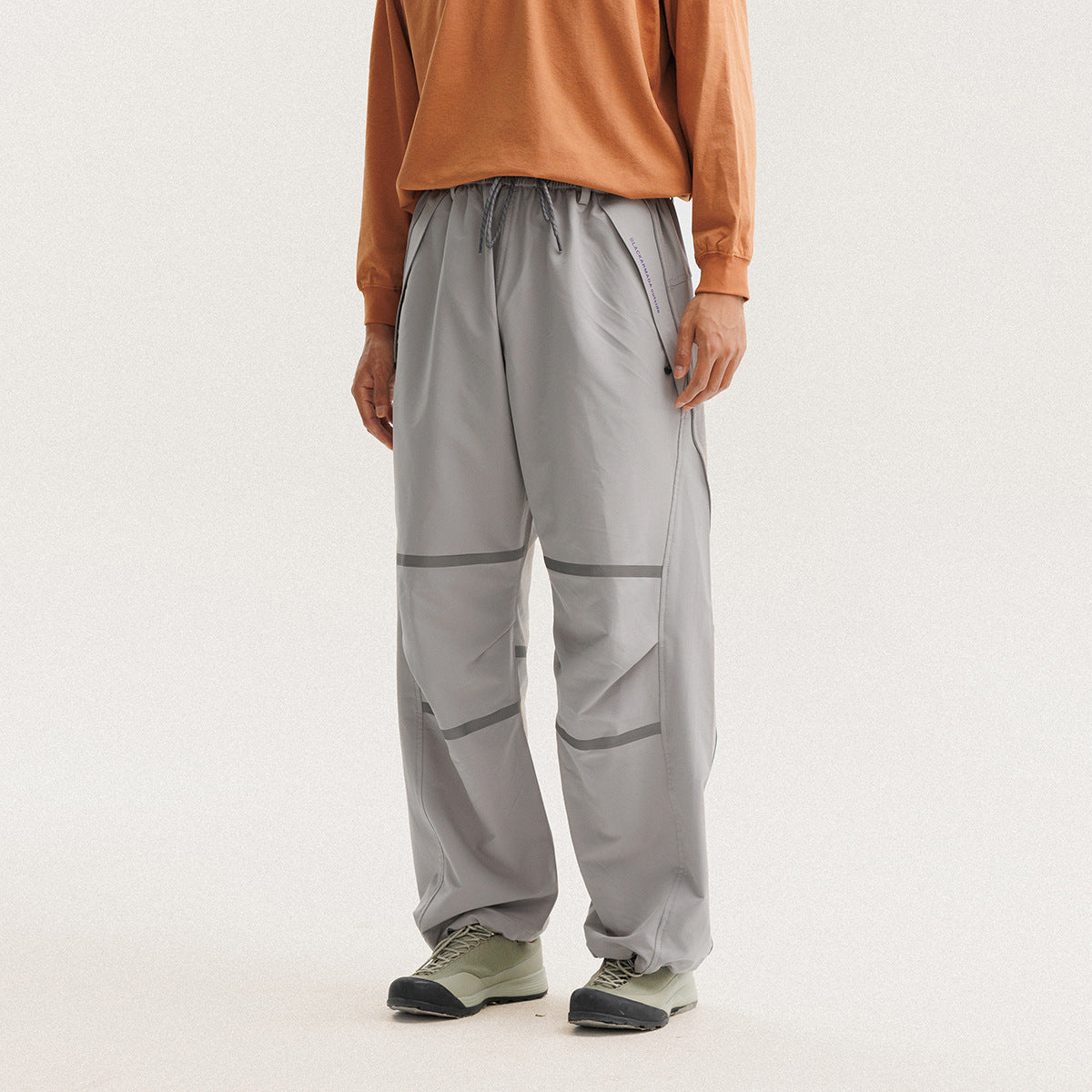 Front view of a model wearing loose gray drawstring pants with dark reflective bands and gathered ankles.