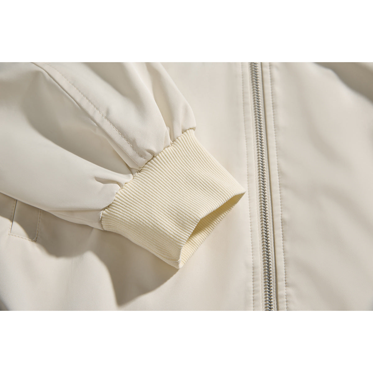Close-up of an ivory jacket's ribbed cuff, sleeve seam, and front zipper.
