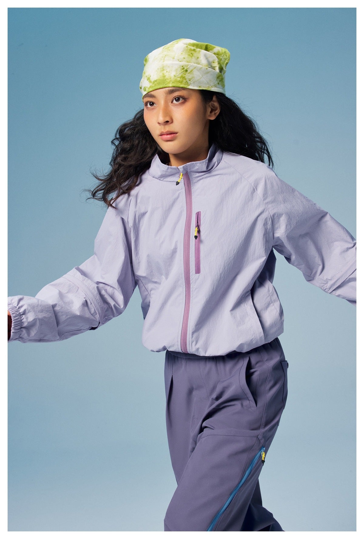 Model in a pale lavender jacket with a stand collar and pink-purple zippers, paired with slate-purple cargo pants.