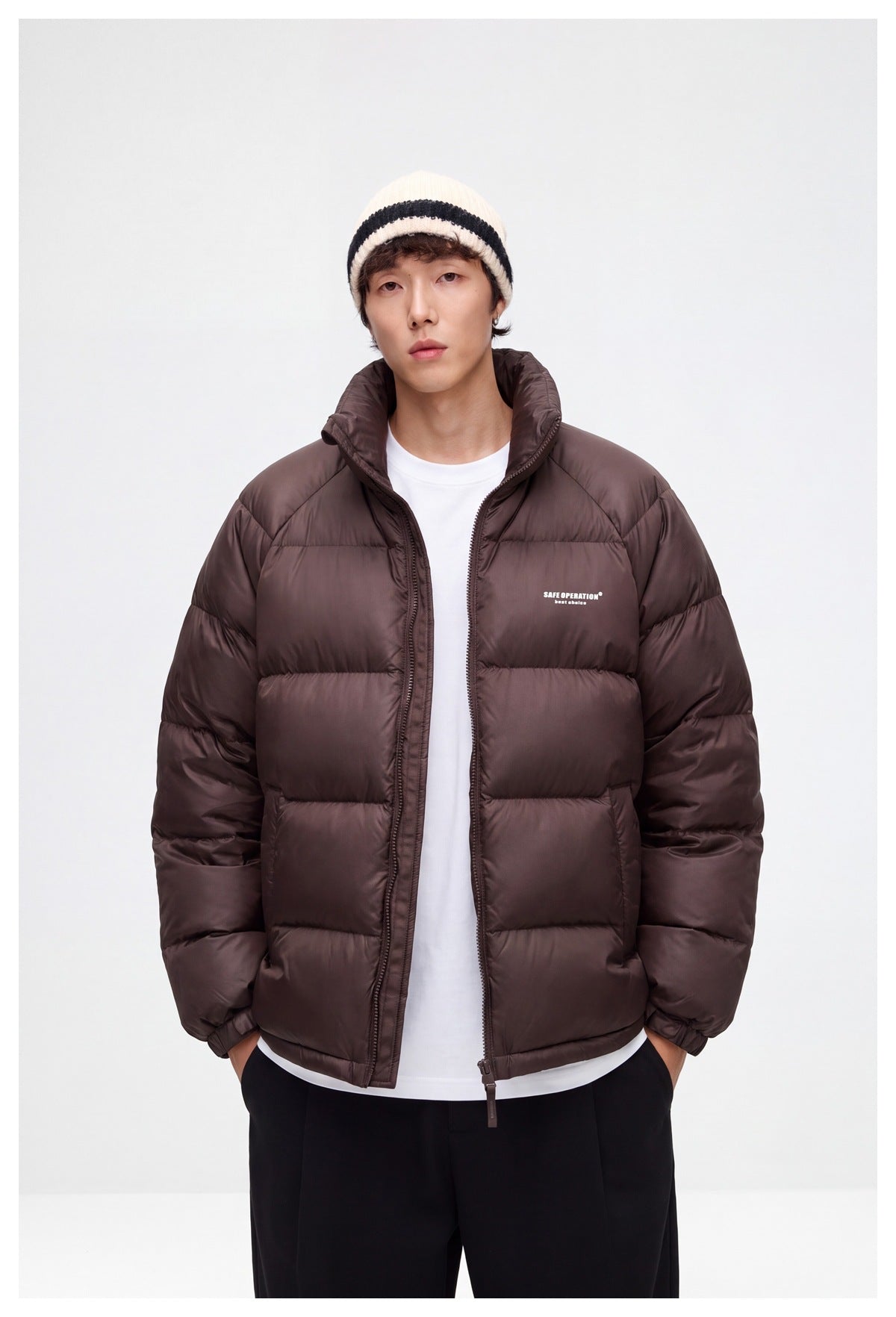 Model wearing a dark brown quilted puffer jacket with a high collar and zip front, layered over a white shirt.