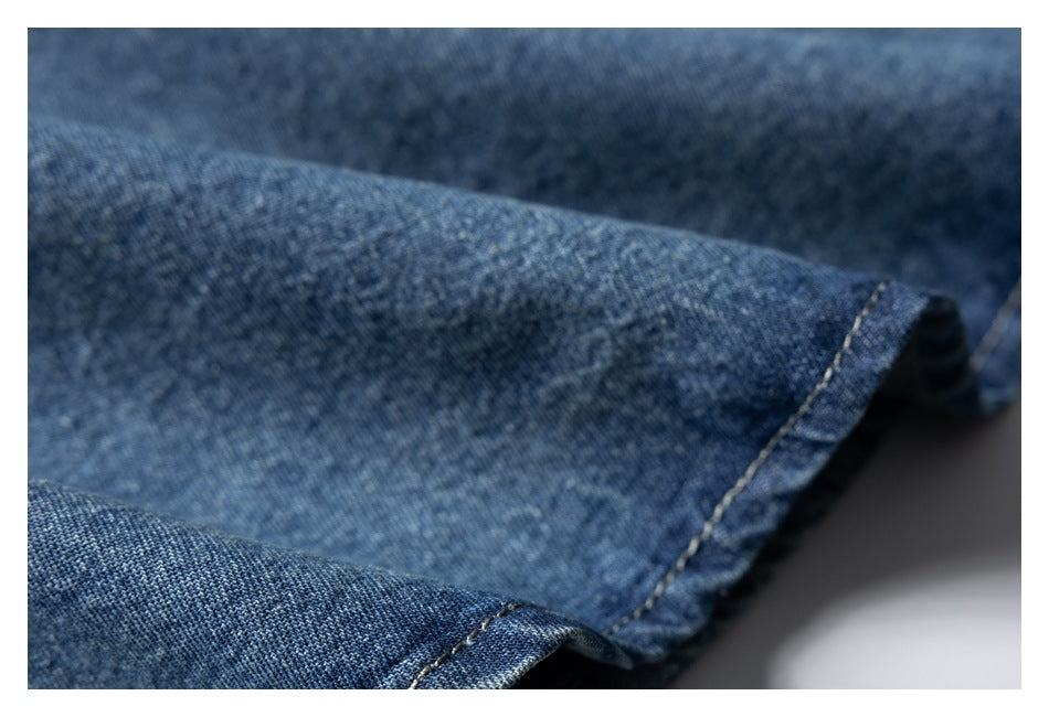 Close-up of blue denim fabric with a folded, light-colored stitched hem.
