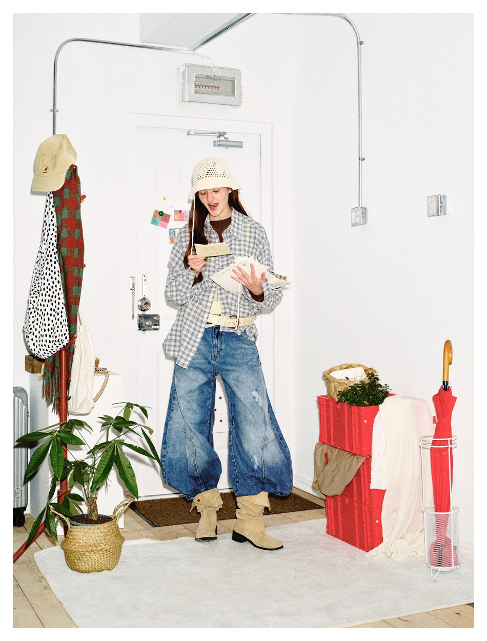 Full-length model wearing a gray-blue plaid button-down shirt, loose blue jeans, cream crochet hat and tan boots.