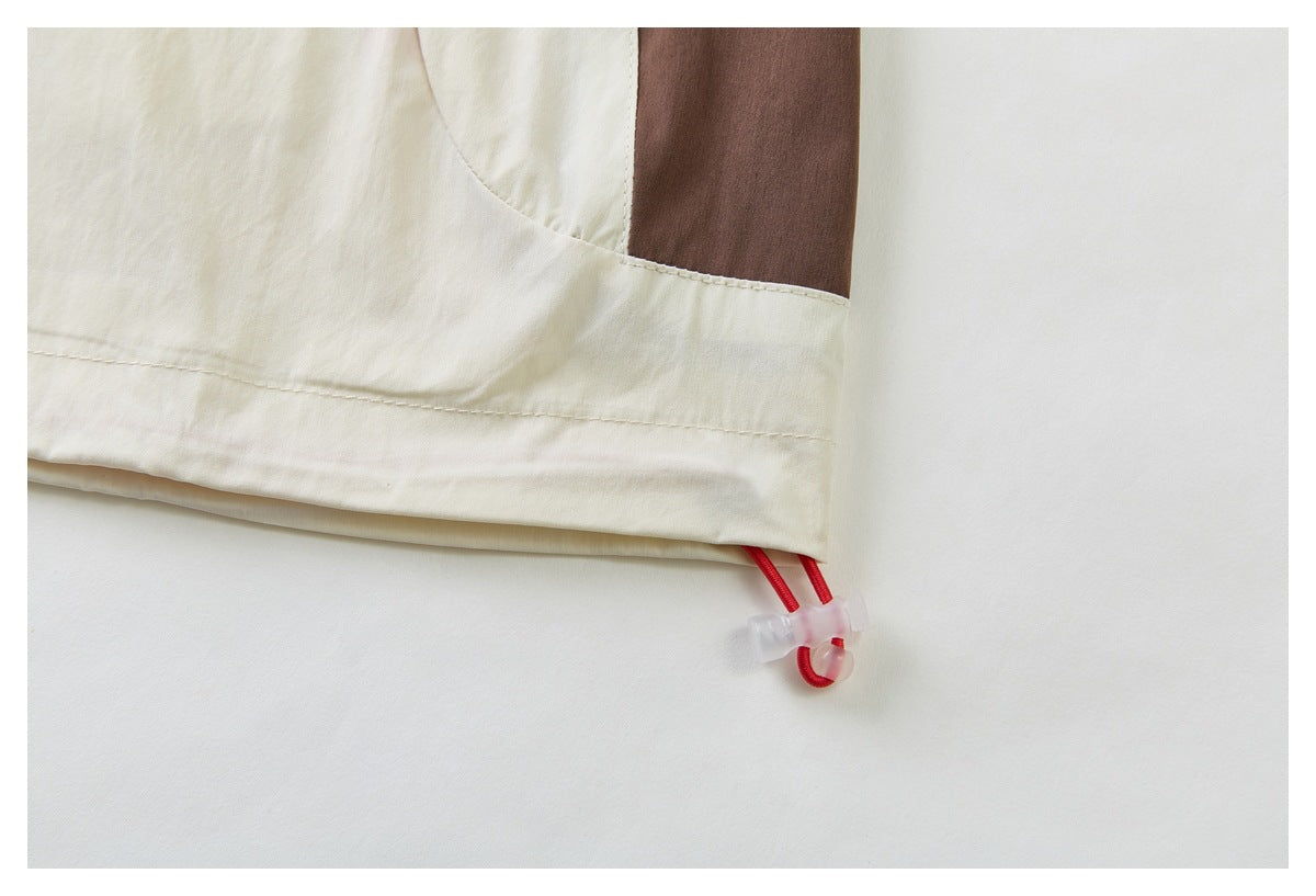 Close-up of a cream garment hem with a red adjustable drawcord and toggle beside a brown panel.
