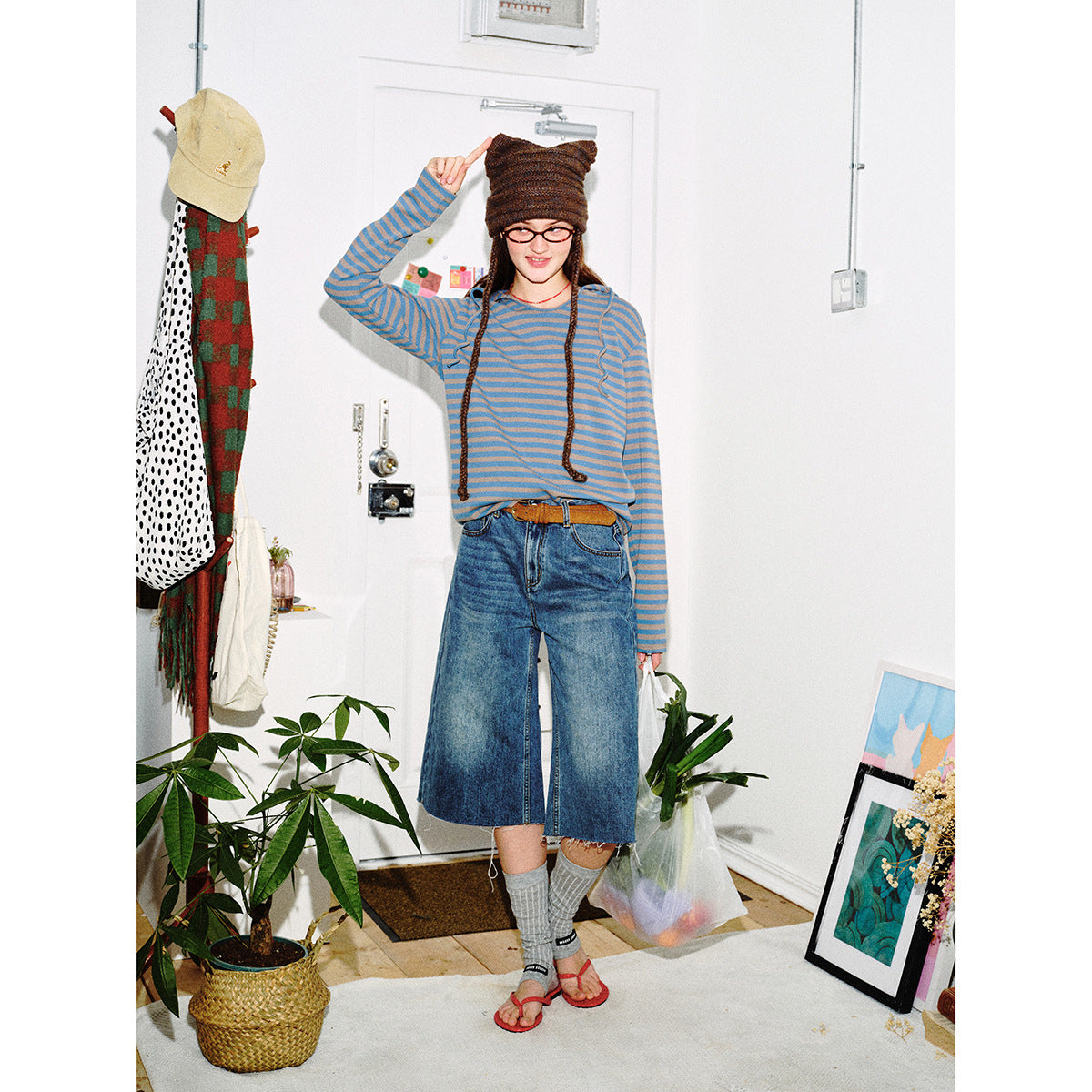 Model wearing a blue and taupe striped hooded top with wide-leg denim culottes, a brown knit hat, and sandals.