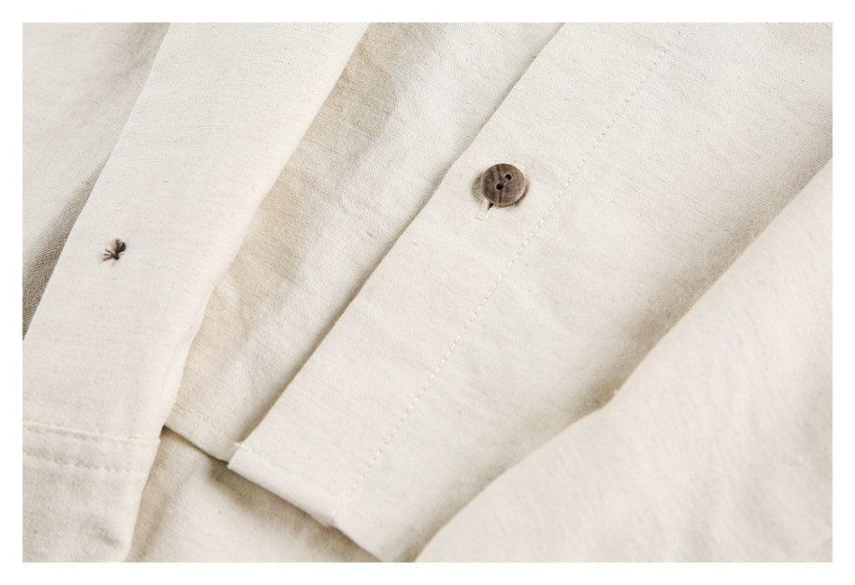 Close-up of an ivory shirt seam with a brown button and a small dark stitch detail.
