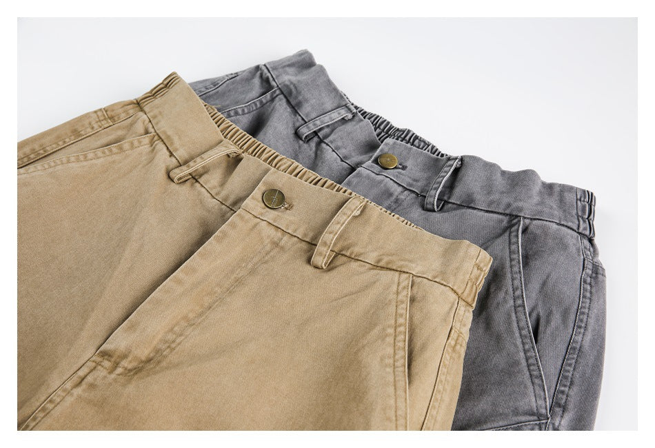 Close-up of tan and charcoal trousers overlapping, showing the front waistbands, belt loops, buttons and seams.