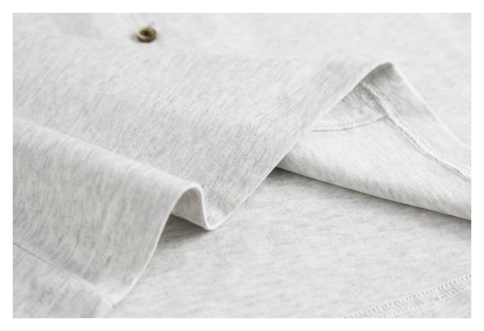 Close-up of a light gray heather shirt with a small brown button and folded, stitched fabric.