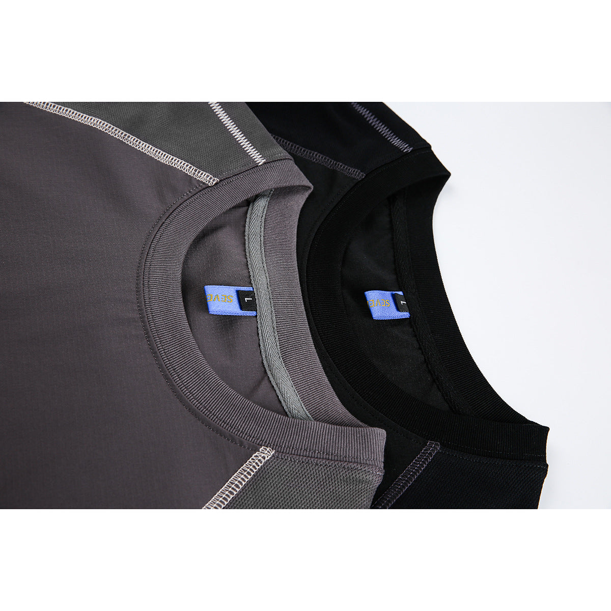 Close-up of gray and black crew-neck T-shirts showing ribbed collars, interior labels and contrast stitching.